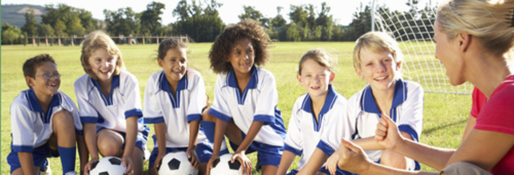 Youth group soccer players in blue and white uniforms smiling at female coach who was hired after receiving a cleared background check.