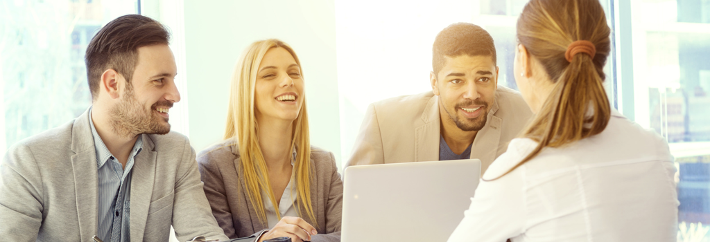 Diverse group of young, professional applicants smiling across the desk at a young woman conducting an interview with focus on the male African-american applicant who provide a completed background check with his application.